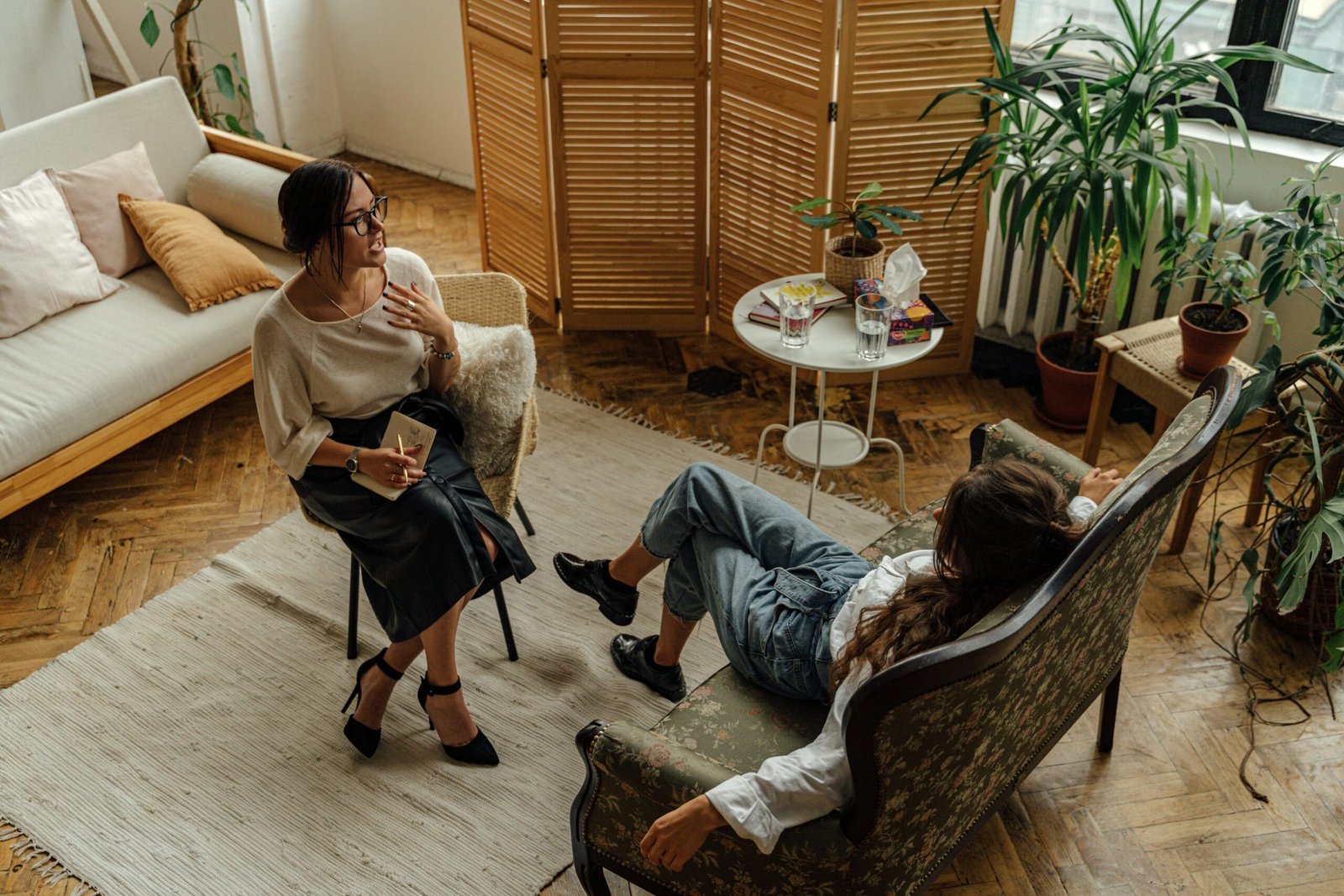 How To Find A Good Therapist Near Me? 1 Two women engaged in a psychotherapy session in a warm, inviting interior with plants and natural lighting.